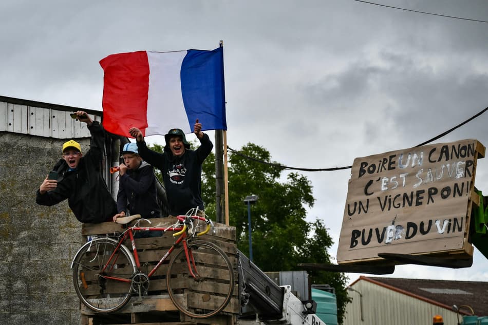 Espectadores comemoram com uma placa que diz 'beba uma taça de vinho salva um produtor de vinho, beba vinho!' ao longo do percurso (foto: Marco BERTORELLO / AFP)