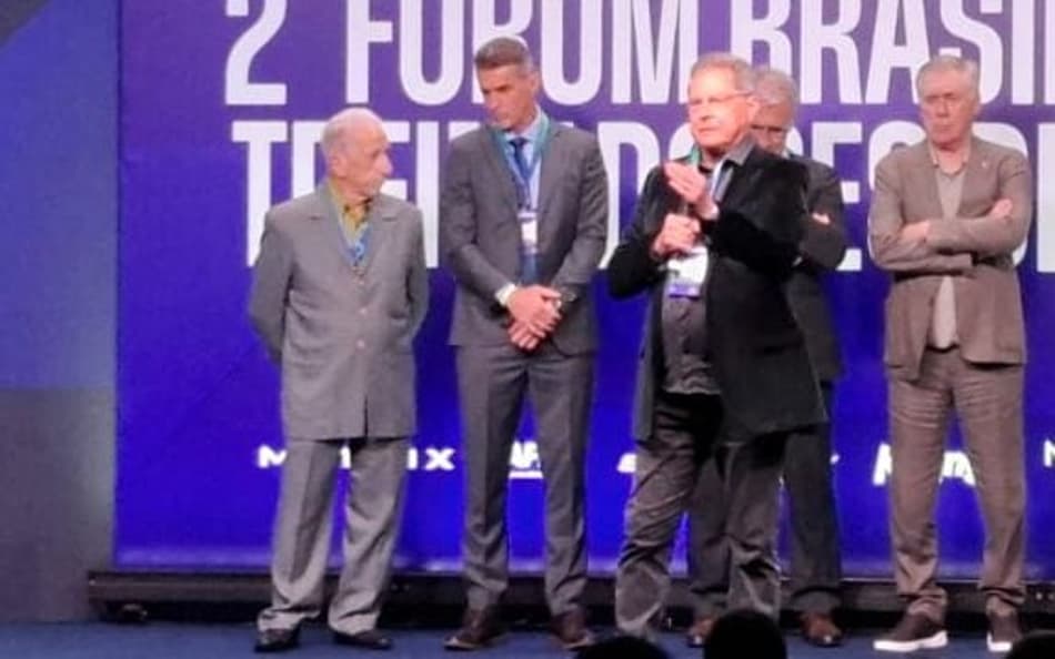 Oswaldo de Oliveira discursa em palco com Carlo Ancelotti