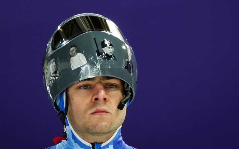 o ucraniano Vladyslav Heraskevych usa capacete com imagens de atletas vítimas da guerra com a Rússia durante treino de skeleton em Cortina. Ele foi desclassificado dos Jogos por se recusar a retirar o item. (Foto: Franck Fife/AFP)