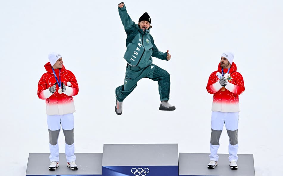 Da esquerda para a direita, Marco Odermatt (prata), Lucas Pinheiro Braathen (ouro) e Loic Meillard (bronze) celebram no pódio do slalom gigante masculino em 2026. (Foto: Fabrice Coffrini/AFP)