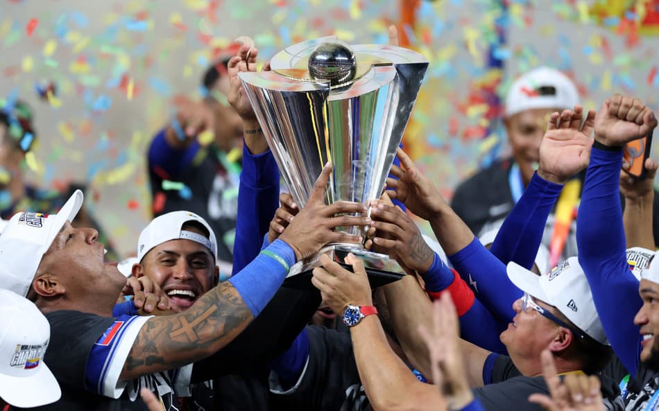 Salvador Pérez e o técnico Omar López erguem o troféu após a vitória da Venezuela por 3 a 2 sobre os Estados Unidos na final do Clássico Mundial de Beisebol, no loanDepot Park, em Miami, em 17 de março de 2026. (Foto: Al Bello/getty images/afp)