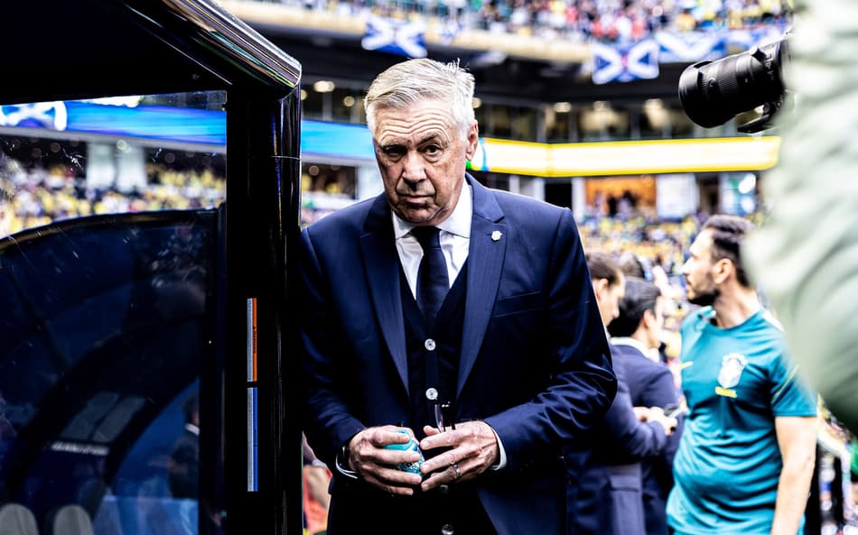 Técnico Carlo Ancelotti em pé ao lado do banco de reservas.