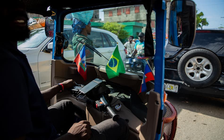 Um homem com bandeiras haitianas e brasileiras em seu veículo dirige em Porto Príncipe, Haiti