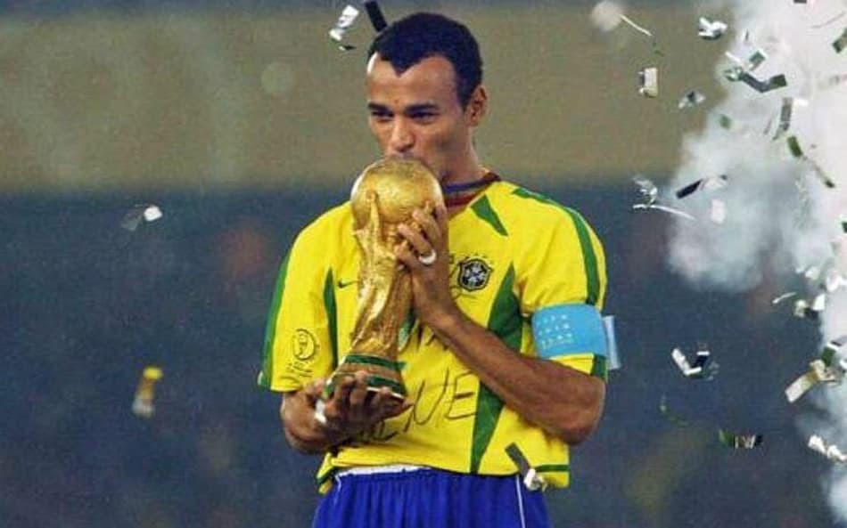 Cafu, com camisa amarela e calção azul, ergue a taça da Copa do Mundo de 2002 pelo Brasil