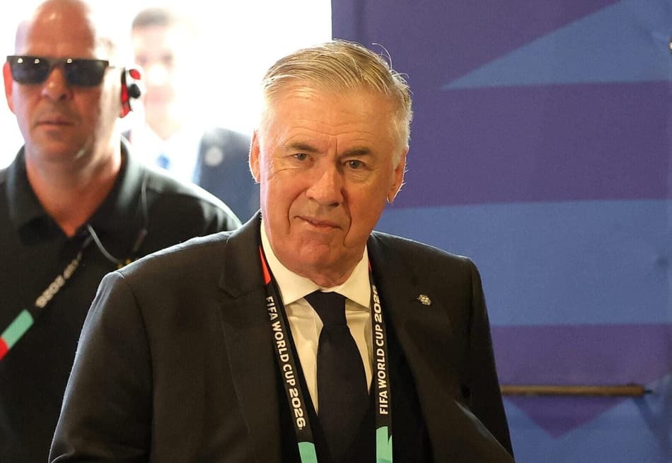 Carlo Ancelotti, técnico da Seleção Brasileira, de terno preto e crachá da Fifa, sorrindo e acenando para os presentes