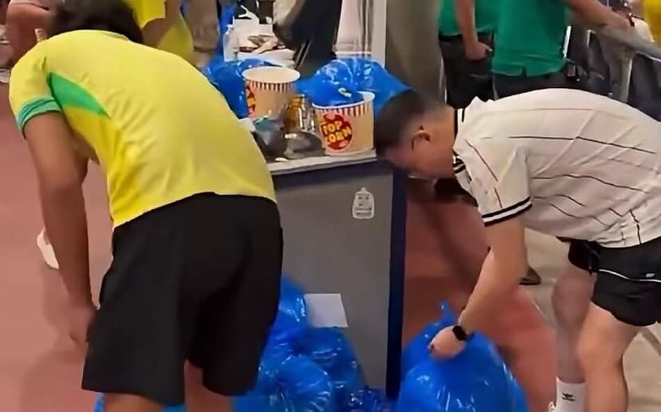 Um torcedor brasileiro, com camisa amarela, ajuda um torcedor japonês, de camisa branca, a recolher o lixo após o jogo da Copa do Mundo