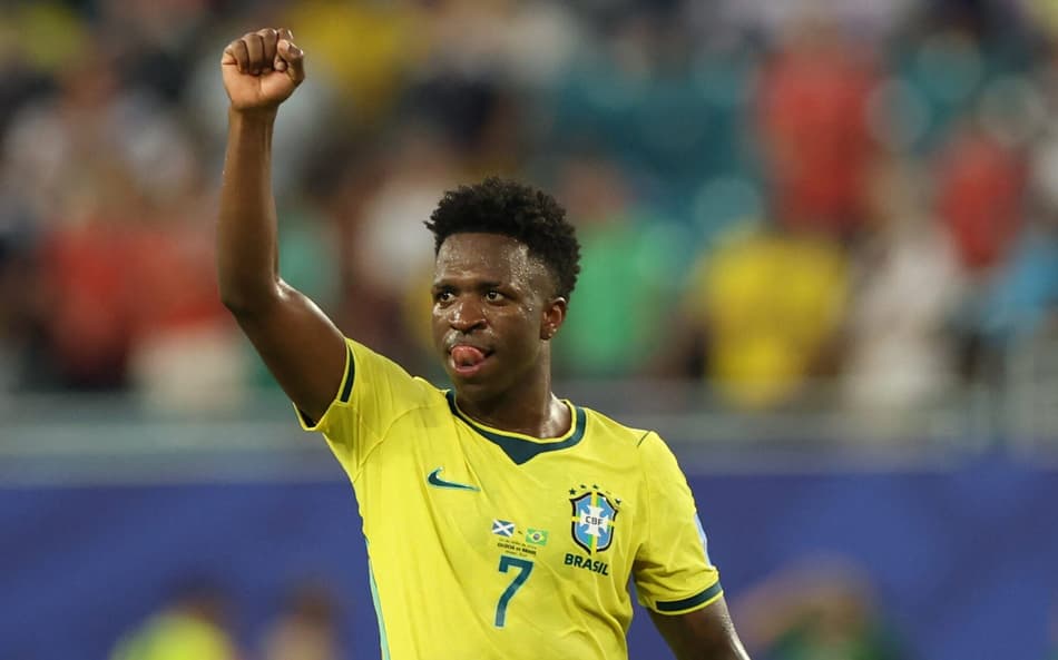 Vinicius Junior, de amarelo, levanta a mão direita em direção ao céu
