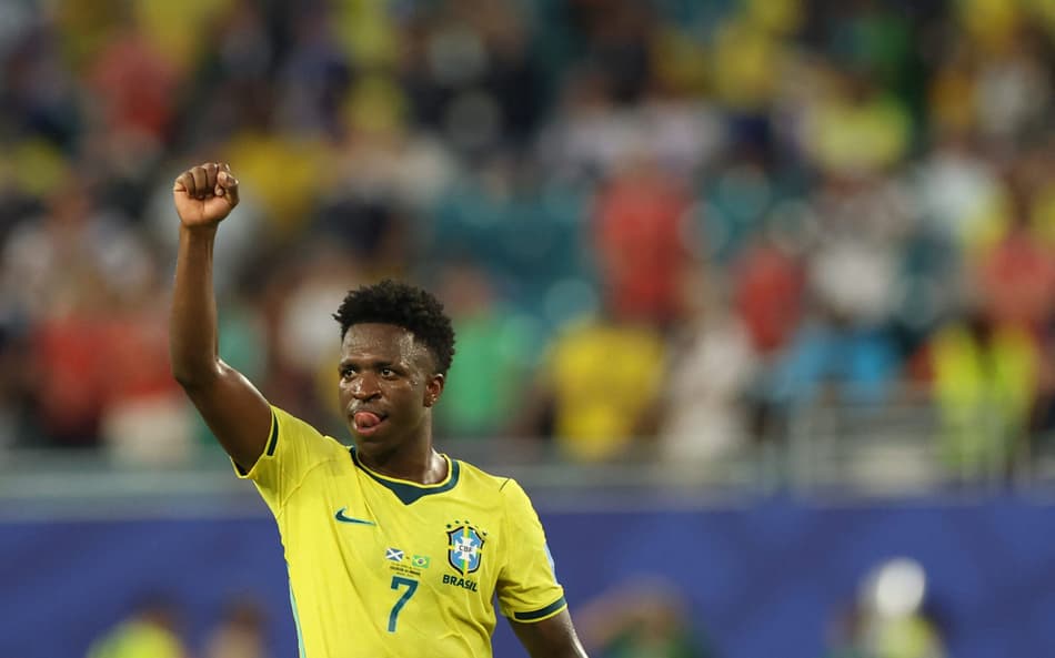 Vinicius Junior, de amarelo, levanta a mão direita em direção ao céu