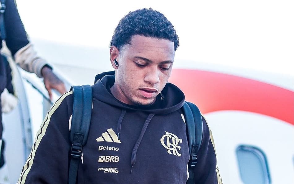 Daniel Sales descendo do avião com fone no ouvido e moletom marrom
