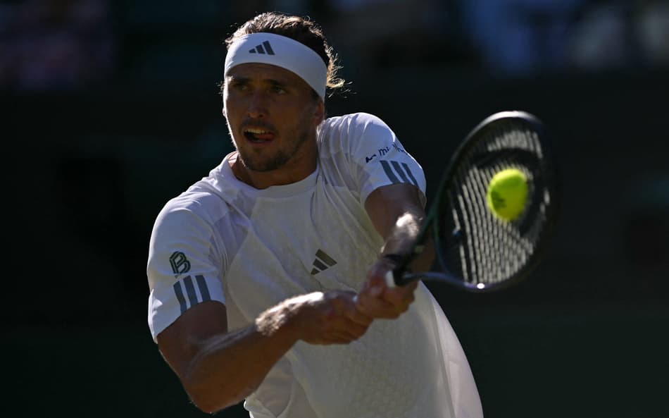Com uma faixa branca na cabeça, Alexander Zverev segura a raquete com as duas mãos e acerta a bola