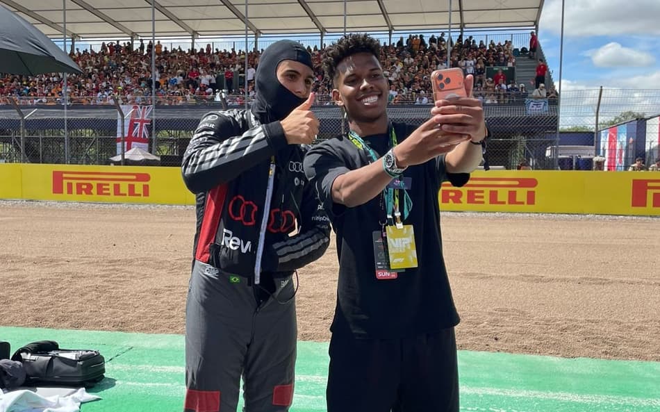 À esquerda, Gabriel Bortoleto, de balaclava e uniforme da Audi, faz um sinal de "joia" com a mão; à direita, Estêvão tira uma selfie com o celular