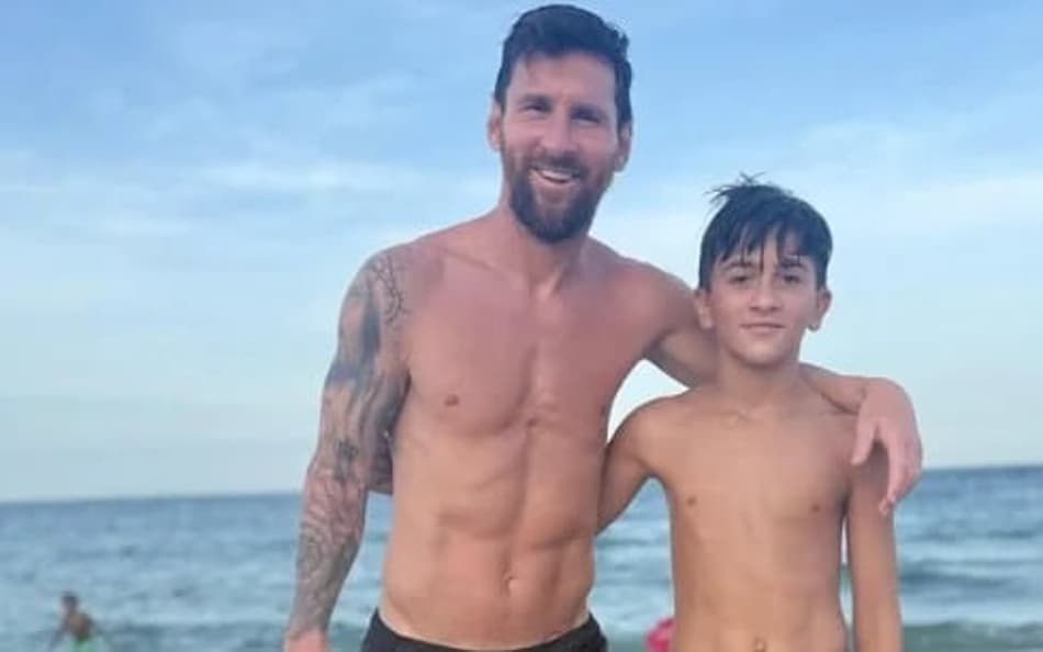 : Messi e o filho mais velho, sem camisa, posam na praia; jogador da Argentina exibe tatuagens no braço.