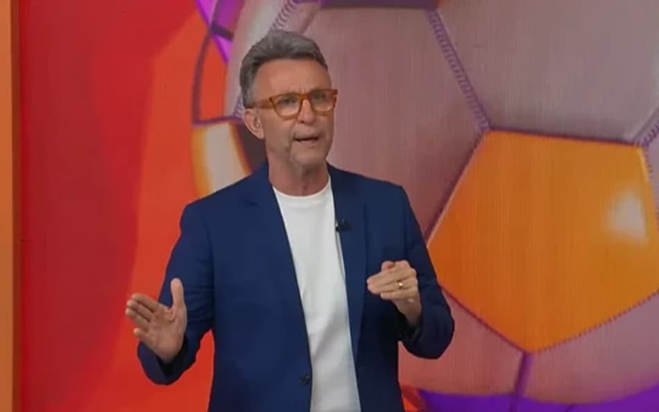 Neto com terno azul e camisa branca durante apresentação do programa